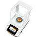 High-angle view of a Sartorius Secura 120 g semi-micro balance showing an orange granular sample in a clear dish on the weighing pan inside the glass draft shield chamber and an active color touchscreen display.
