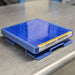 Three-quarter angled studio view of a blue Scienceware Spindrive orbital shaker platform resting on a metallic work surface, showing its flat platform top with a non-skid surface and caution label