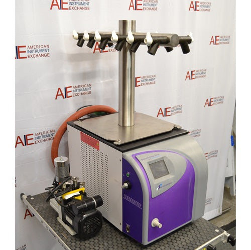 An angled side view of an SP Scientific BenchTop Pro freeze dryer sitting on a benchtop, showing the purple front control panel, side ventilation panel, top multi-port tree manifold, orange vacuum hose, and an attached vacuum pump in the foreground.