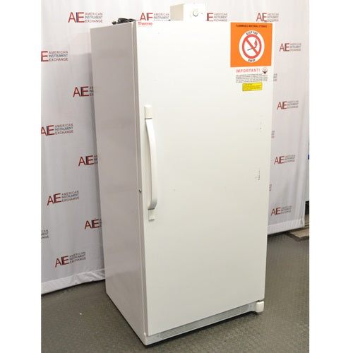 An angled side view of a white Thermo Scientific 3552-10A flammable material storage freezer, showing the vertical door handle on the front left, top-mounted control dial, and orange safety warning label on the upper right against an American Instrument Exchange backdrop.