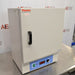 An angled side view of a closed Thermo Scientific PR305225M Precision mechanical convection oven resting on a stainless steel surface in front of an American Instrument Exchange backdrop, highlighting the left casing panel, serial label, front door handle, top Thermo Scientific branding, and bottom blue control panel.
