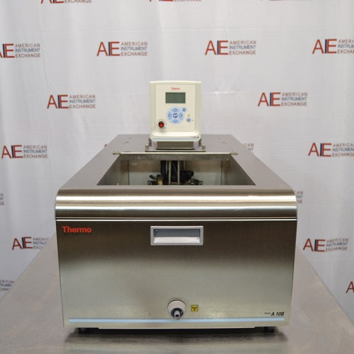 A head-on front view of a Thermo Scientific A10B refrigerated bath circulator sitting on a metal workbench in front of an American Instrument Exchange backdrop, displaying its stainless steel front panel, drain valve, open bath area, and top-mounted digital control head.