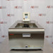 A head-on front view of a Thermo Scientific A10B refrigerated bath circulator sitting on a metal workbench in front of an American Instrument Exchange backdrop, displaying its stainless steel front panel, drain valve, open bath area, and top-mounted digital control head.