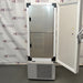  Straight-on studio view of a Thermo Scientific TSX40086 upright ultralow temperature freezer standing on a grey floor against a branded backdrop, featuring a solid grey outer door, ergonomic handle, integrated blue digital touchscreen interface, TSX Series branding, and a lower perforated ventilation panel
