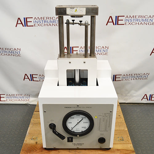 An SLM Aminco French press, primarily white and silver in color, with pressure adjustment dials and a logo on the side, placed against a white background with 'American Instruments' logo in the top corner.