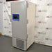Straight-on studio view of a Thermo Scientific TSX40086 upright ultralow temperature freezer standing on a grey floor against a branded backdrop, featuring a solid grey outer door, ergonomic handle, integrated blue digital touchscreen interface, TSX Series branding, and a lower perforated ventilation panel