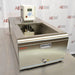 A top-angled front view of a Thermo Scientific A10B refrigerated bath circulator resting on a metal surface against an American Instrument Exchange backdrop, showing the open bath chamber with internal cooling coils, top-mounted digital control unit, stainless steel front casing, drain valve, and model logo.