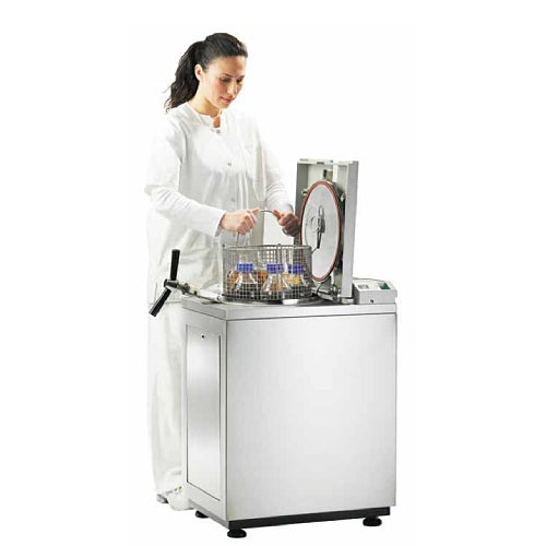 Laboratory technician loading a Tuttnauer vertical top-loading autoclave with a wire basket of glass flasks.