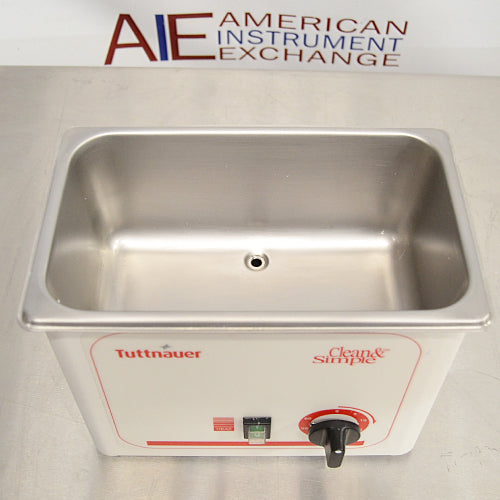 Elevated front view of a Tuttnauer Clean & Simple CSU1H ultrasonic cleaner showing the empty stainless steel cleaning basin, central drain port, and front control switches.