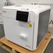 Angled view of a Tuttnauer T-Edge 11B tabletop autoclave showing the front touchscreen, door handle, and right-side ventilation grille.