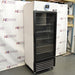 Three-quarter left-angled studio view of a VWR HCLS-26 upright laboratory refrigerator standing on casters against a branded backdrop, featuring a glass door with a black frame, top-mounted digital display console, and louvered bottom grille