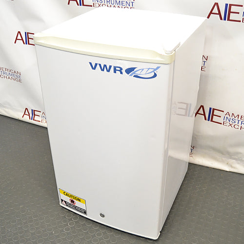 A white VWR undercounter laboratory refrigerator with a blue logo, standing on a floor with 'CAUTION' and 'SERVICE内部使用禁止' stickers on it.