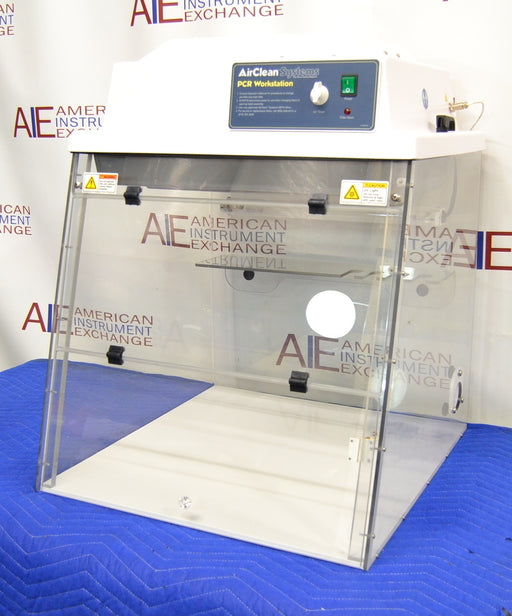 Front eye-level view of an AirClean Systems AC624LFUV PCR workstation sitting on a blue protective cloth, highlighting its clear acrylic enclosure, folding front sash, and digital-free control panel housing
