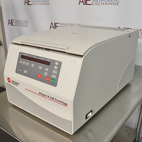 Left angled perspective view of a Beckman Coulter Allegra X-22R refrigerated centrifuge on a stainless steel surface, featuring its beige housing, closed lid, digital control panel, and side power switch