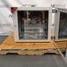 Front view of a Binder FD-S 115 mechanical convection oven with its side-hinged door swung open, showing the polished stainless steel interior chamber, adjustable wire shelves, and a reflective back panel