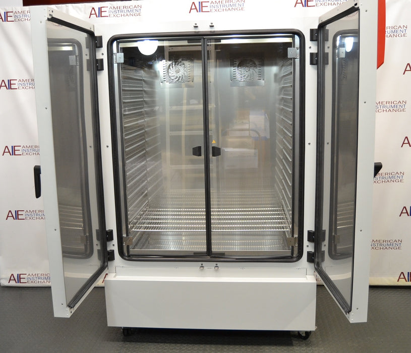 Front eye-level view of a Binder KMF 720 constant climate and humidity test chamber with its double outer doors swung open to reveal internal glass doors, stainless steel chamber interior, and wire shelving racks