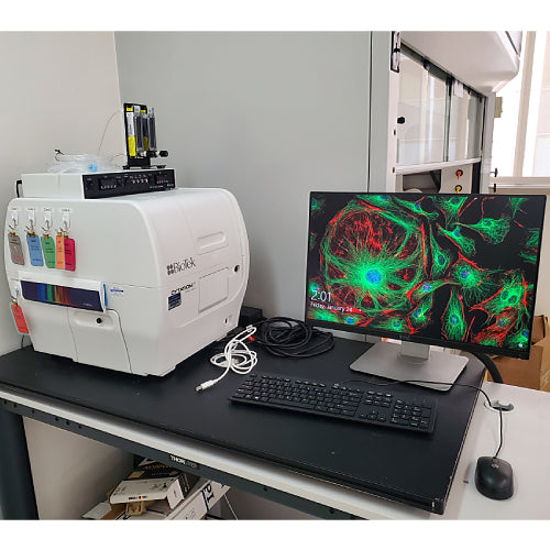 Front eye-level view of a BioTek Cytation 5 cell imaging multimode reader set up on a laboratory desk with an attached monitor displaying a fluorescent cell image, keyboard, mouse, and control module