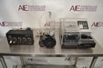 Front eye-level view of a BioTek ELx405UV Select microplate washer system resting on a stainless steel table, complete with its accompanying valve module, vacuum pump, and fluid bottle setup
