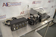 Right angled perspective view of a BioTek ELx405UV Select microplate washer system showcasing its valve module, cables, vacuum pump, and washer unit on a stainless steel tabletop