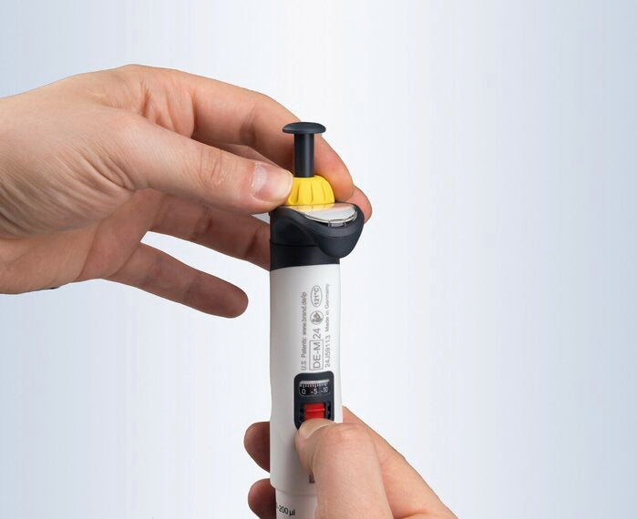 Close up of user hands adjusting volume wheel and setting lock on BRANDTECH Transferpette pro pipette with yellow accent top