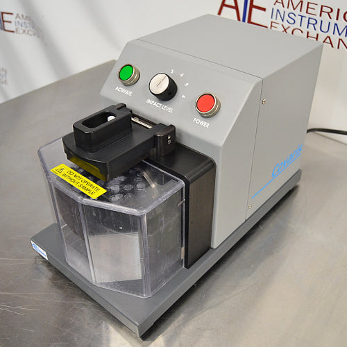Left three-quarter angle product view of a Covaris cryoPREP CP02 dry pulverizer, featuring its grey housing, clear protective safety shield, impact level dial, and top control buttons