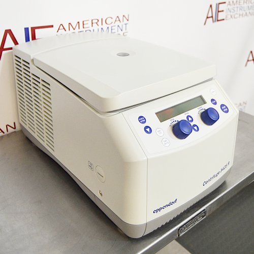 Front angled perspective view of an Eppendorf 5425R refrigerated microcentrifuge on a stainless steel surface, featuring its light grey housing, closed lid, side cooling vents, and front control panel with blue knobs