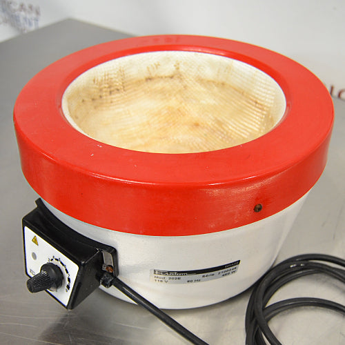 Left three-quarter angle product view of a Fisatom laboratory heating mantle, showing its red top rim, white body, integrated control box with power dial, specifications label, and power cord on a lab bench