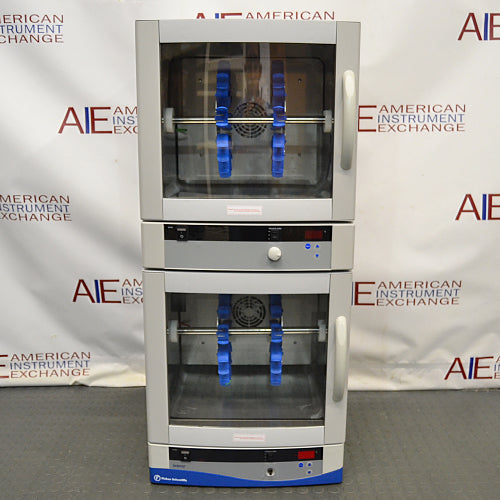 Front product view of a Fisher dual chamber hybridization incubator against a branded backdrop, highlighting its stacked design, two glass-window doors with vertical handles, internal rotating bottle racks, and digital control panels