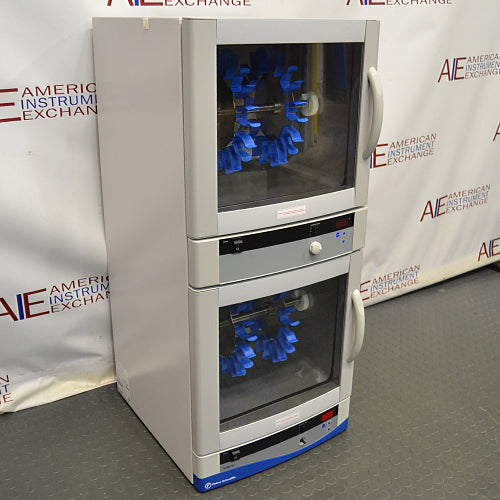 Three-quarter angle view of a Fisher dual chamber hybridization incubator, showcasing its stacked design, dual glass doors with side handles, internal rotating blue bottle rotisserie carousels, and control interfaces
