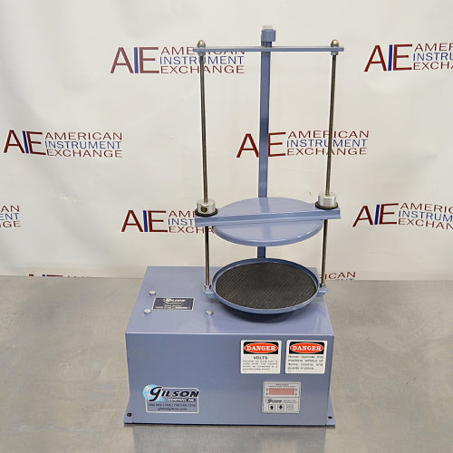 Straight-on front view of a Gilson 8-inch sieve shaker, featuring its blue cabinet housing, vertical clamping rods, safety warning labels, brand logo, and control interface on a stainless steel lab bench