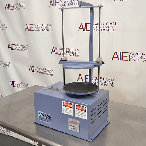 Three-quarter angle product view of a Gilson 8-inch sieve shaker, highlighting its blue housing, vertical clamping rods, timer control panel, and testing platform on a stainless steel lab bench