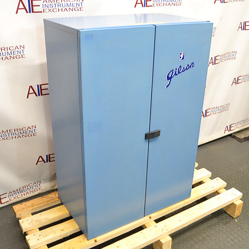 Three-quarter angle product view of a closed blue Gilson sound enclosure cabinet for a sieve shaker, featuring double doors, the Gilson brand logo, and a center latch handle resting on a wooden pallet base