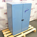 Three-quarter angle product view of a closed blue Gilson sound enclosure cabinet for a sieve shaker, featuring double doors, the Gilson brand logo, and a center latch handle resting on a wooden pallet base