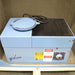 Front product view of a Gilson sieve shaker housed inside a sound enclosure, showcasing its blue housing, brand logo, safety and danger labels, and control dial on a wooden pallet base