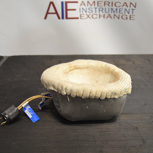 Front product view of a Glas-Col 1L laboratory heating mantle, showing its soft-sided fabric housing, internal heating well, and attached power cord with plug on a dark workbench