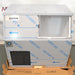Front eye-level view of a new-in-box Hoshizaki F300BAF flaker ice maker resting on a wooden pallet, featuring stainless steel housing covered in protective blue-printed film, a lower front louvered vent, and an open bin door