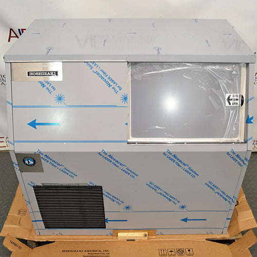 Straight-on front view of a new-in-box Hoshizaki F300BAF flaker ice maker on a wooden shipping pallet, showing protective film wrapping on the stainless steel body, lower black louvered grill, and front access door
