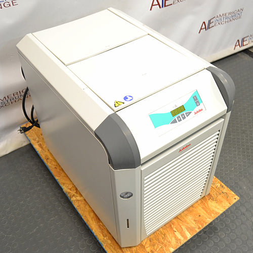 Left three-quarter angle product view of a Julabo FL1701 recirculating chiller, highlighting its white and gray housing, angled digital control panel, lower vented louvered door, and power cord on a wooden pallet base