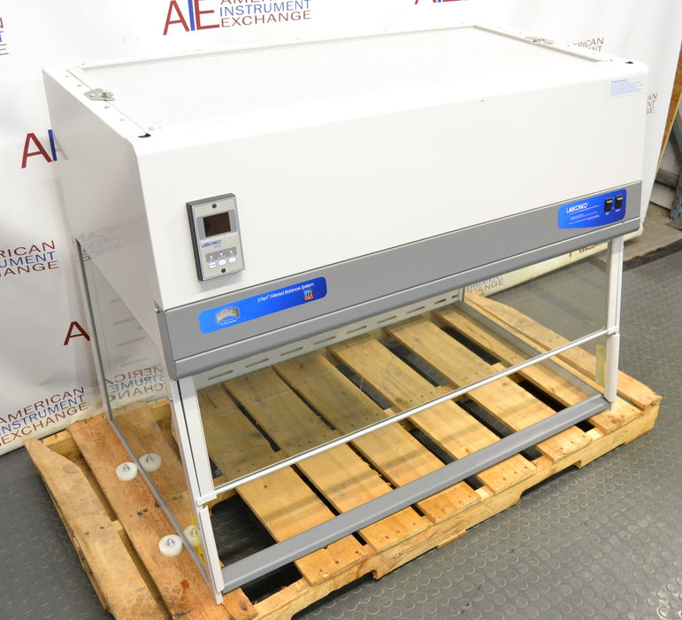 Left angled perspective view of a Labconco XPert Filtered Balance System on a wooden shipping pallet, showing its top filter housing, digital control module, and clear protective enclosure