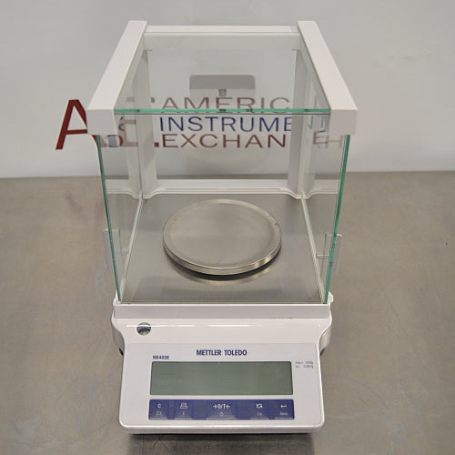 Mettler Toledo ME403E precision balance ka front view, jisme glass draft shield enclosure, stainless steel weighing pan, digital LCD display, aur front control keypad saaf dikhai de rahe hain.   