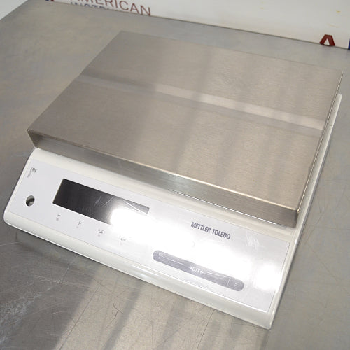 Left three-quarter angle product view of a Mettler Toledo MS12001L/03 high-precision toploading balance, showing its stainless steel weighing pan, white housing, digital control screen, and keypad on a stainless steel bench