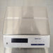 Top-down product view of a Mettler Toledo MS12001L/03 high-precision toploading balance, featuring a large flat stainless steel weighing platter, white base housing, digital display screen, and control panel on a stainless steel surface