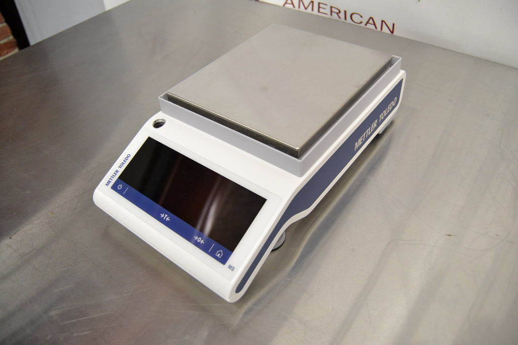 Side angled perspective view of a Mettler Toledo MS3002TS precision balance resting on a stainless steel surface highlighting the branded side panel and weighing platform