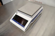 Side angled perspective view of a Mettler Toledo MS3002TS precision balance resting on a stainless steel surface highlighting the branded side panel and weighing platform