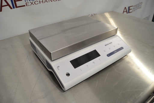 Angled perspective view of a Mettler Toledo MS32001L precision balance on a stainless steel surface, featuring its rectangular stainless steel pan, side panel housing, and front digital readout interface