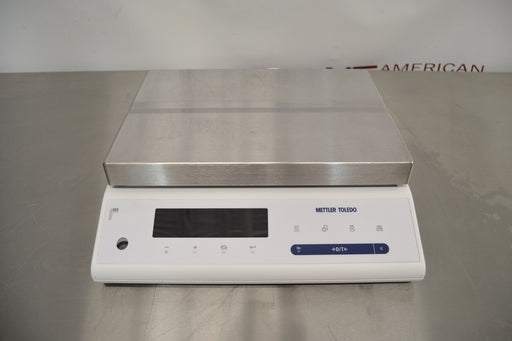 Front eye-level view of a Mettler Toledo MS32001L precision balance resting on a stainless steel surface, showcasing its large stainless steel weighing pan and digital display control panel