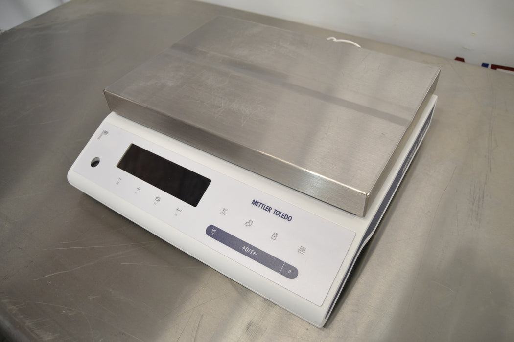 Left elevated angled view of a Mettler Toledo MS32001L precision balance resting on a stainless steel counter, featuring its flat stainless steel weighing platform and front digital display interface