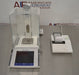 Front high-angle view of a Mettler Toledo XP205 analytical balance on a stainless steel counter, featuring its glass draft shield, separate touchscreen terminal, weighing pan, and a connected laboratory printer