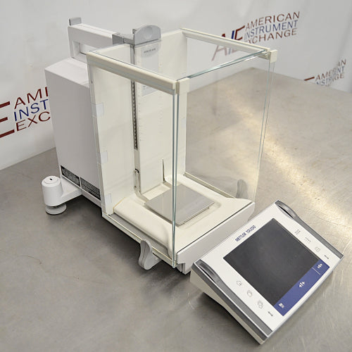 Mettler Toledo XP504 analytical balance ka left angle view, jisme glass draft shield ka left side, weighing chamber, aur separate digital control terminal stainless steel table par rakhe hue saaf nazar aa rahe hain.   
