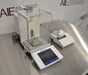 Angled perspective view of a Mettler Toledo XPE205 analytical balance resting on a stainless steel surface, featuring its protective glass draft shield, separate touchscreen control terminal, weighing pan, and attached laboratory printer